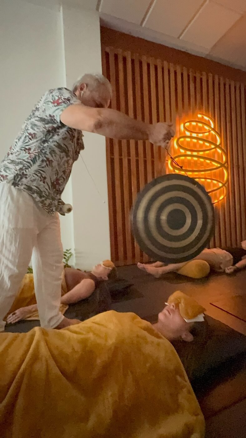 Sam Cutri using a gong during a live Soundful Experience with participants resting on mats